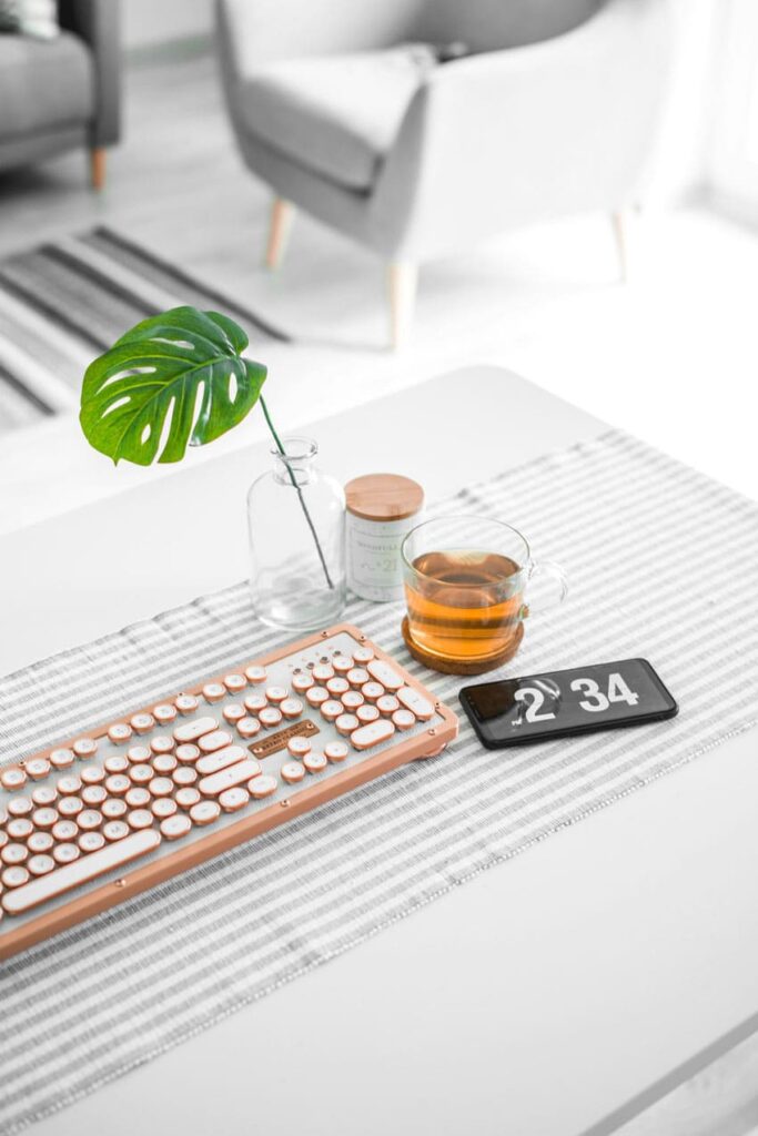 an aesthetic white and pink keyboard, cup of tea and cellphone over a office desk