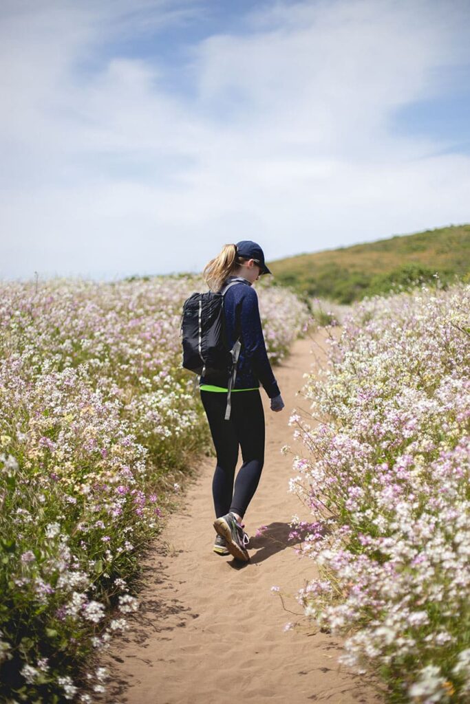a woman in sport clothes and with a backpack waking along a trail in natural landscape