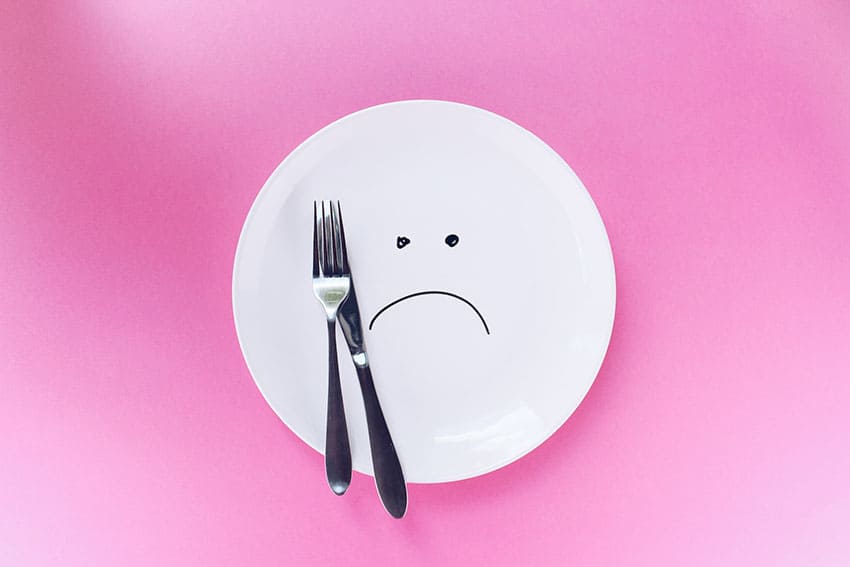 an empty dish with a sad face drawing in the middle of it plus a fork and a knife
