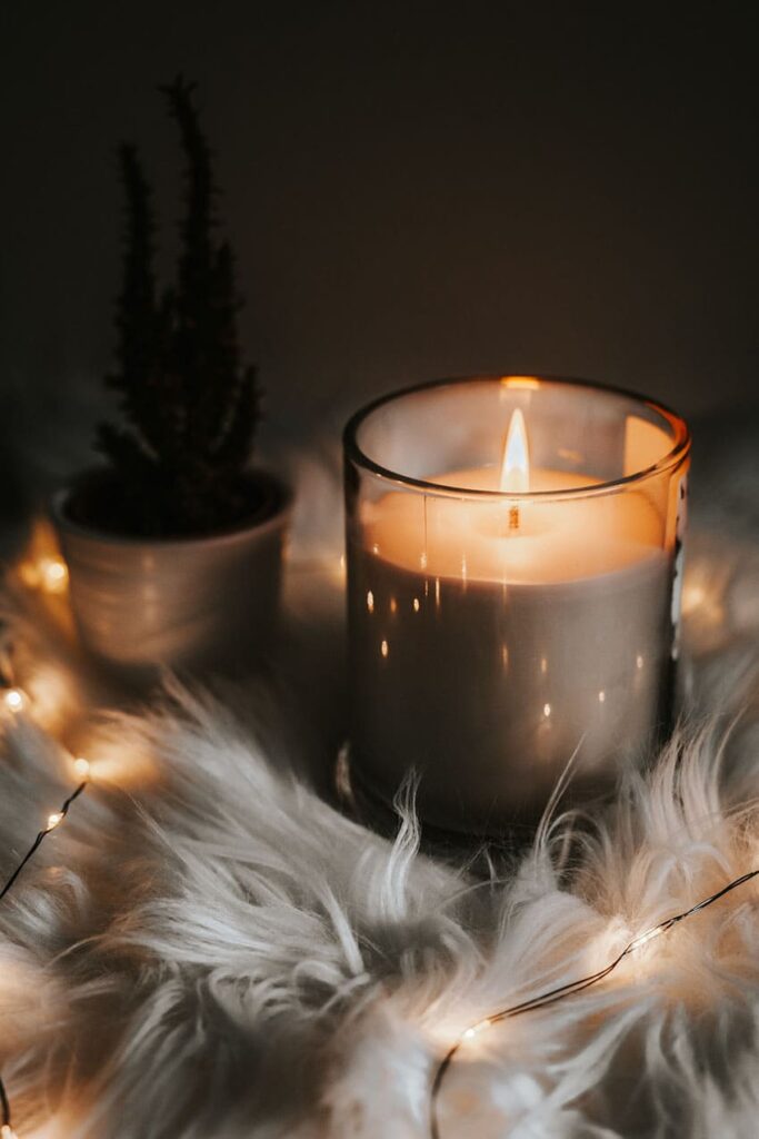 a grey candle over a soft fabric and a small plant with cozy lights
