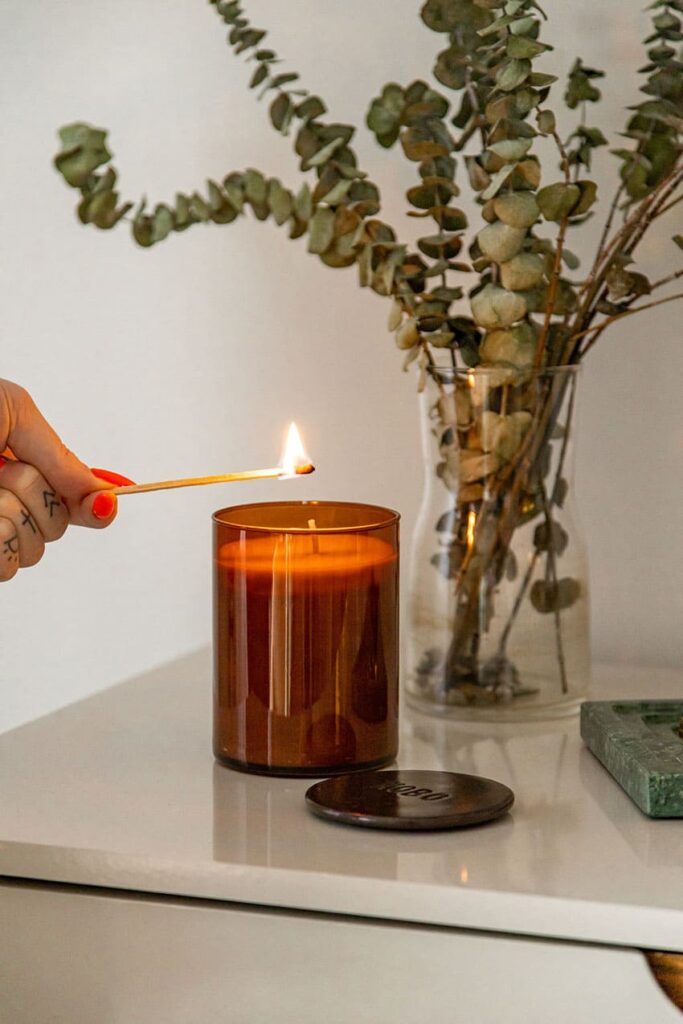 a woman lighting a candle a transparent vase holding olive branches in the background