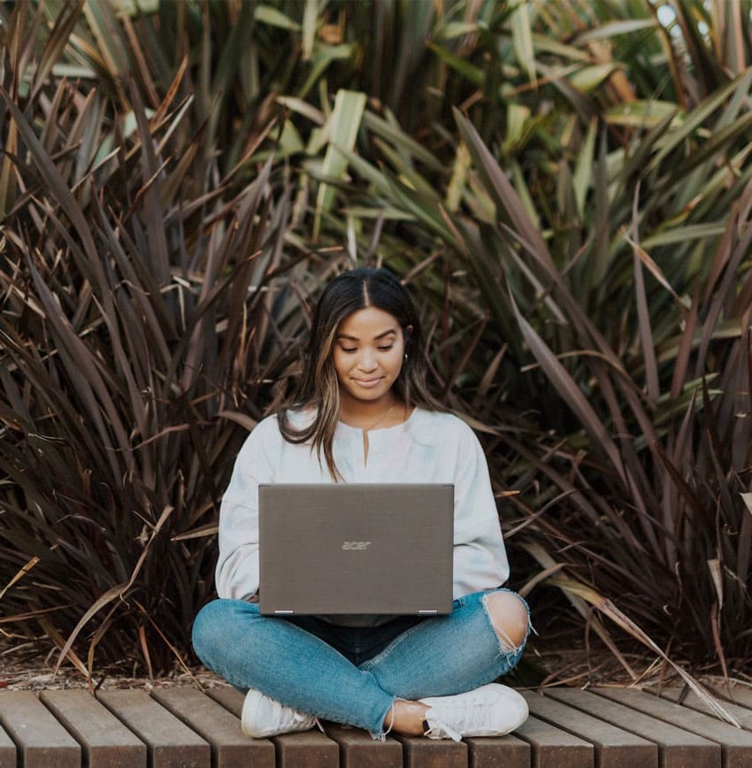 a-woman-outside-her-house-sitting-on-a-deck-and-using-a-laptop-how-to-sell digital-planners-on-etsy