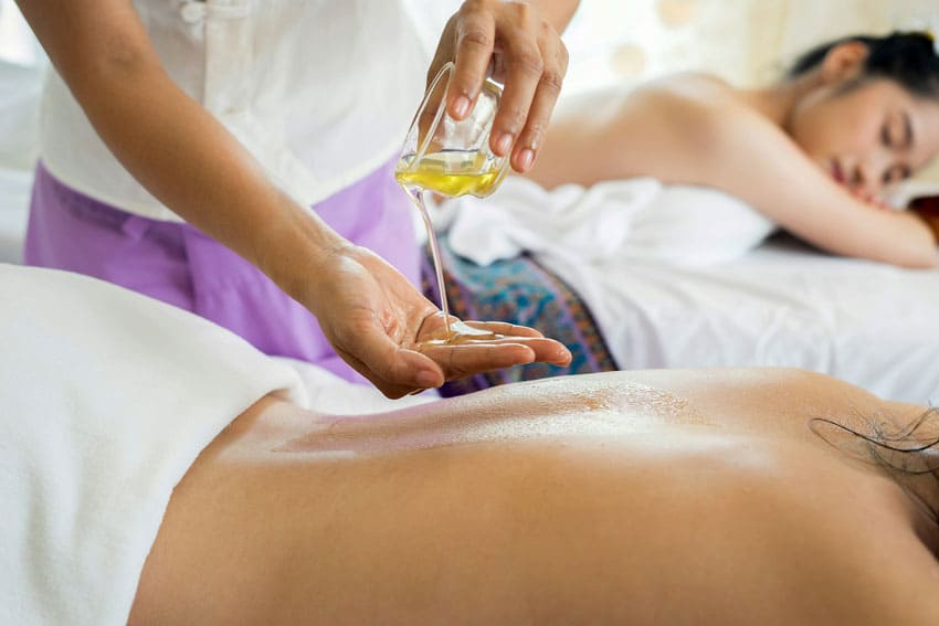a woman puttin oil on her hand to give massage to another woman. an asian woman on the background waiting for her turn spa party planner as one of the best beauty side hustles