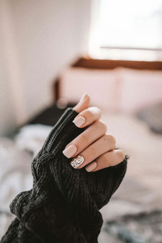 a woman's hand with nails done, neutral colors nail tech as one of the best beauty side hustles