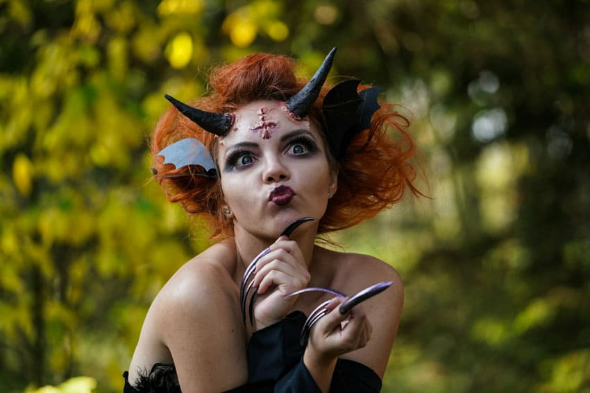a young woman with halloween makeup wearing horns, long nails and fake wounds