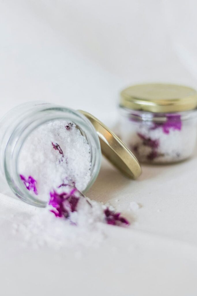 two containers one open the other one closed with white sea salts and purple flowers bath salts seller as one of the best beauty side hustles
