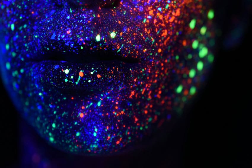 foregrounf shot of woman's mouth with glow in the dark painting all over her face and lips