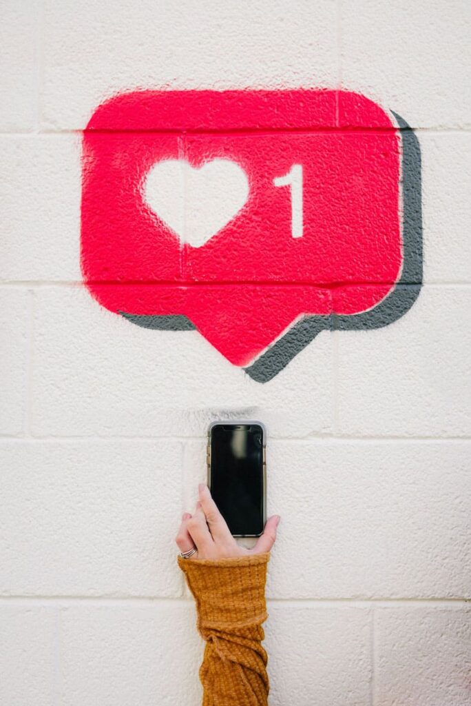 a woman holding a cellphone over a white wall and a like Instagram notification painted over the wall