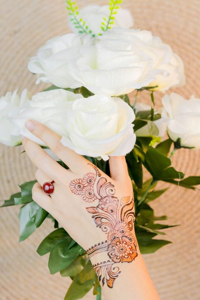 a woman's hand with henna tattoo on it holding white roses