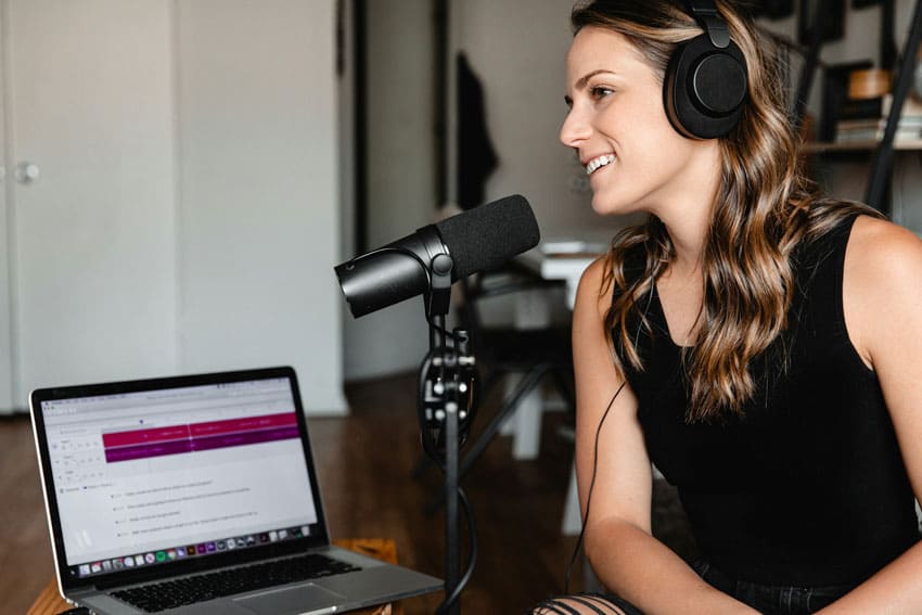 a brunette woman wearing headphones and recording a podcast with her microphone and laptop beauty podcaster as one of the best beauty side hustles