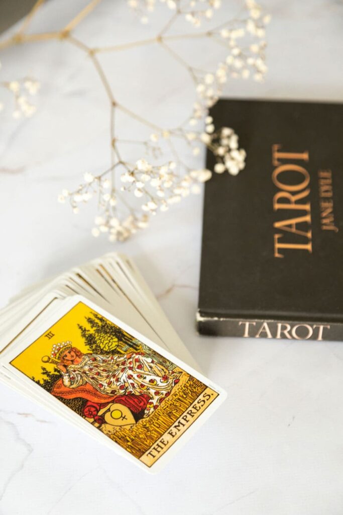 tarot cards, a tarot books and white flowers, tarot reading as one of the best beauty side hustles