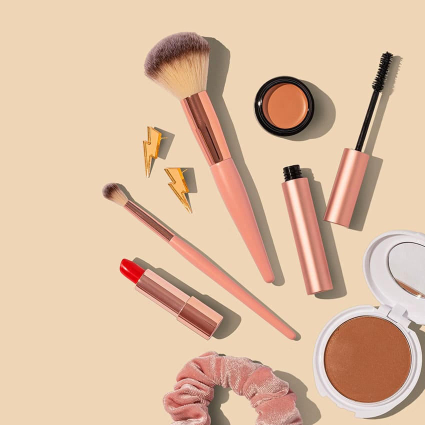makeup items and brushes over a nude color surface