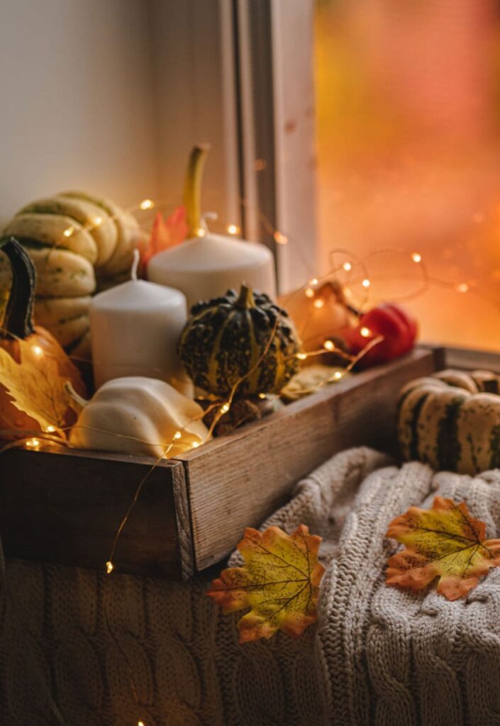 a wooden box with pumpkins and candles and a knitted sweater next to it