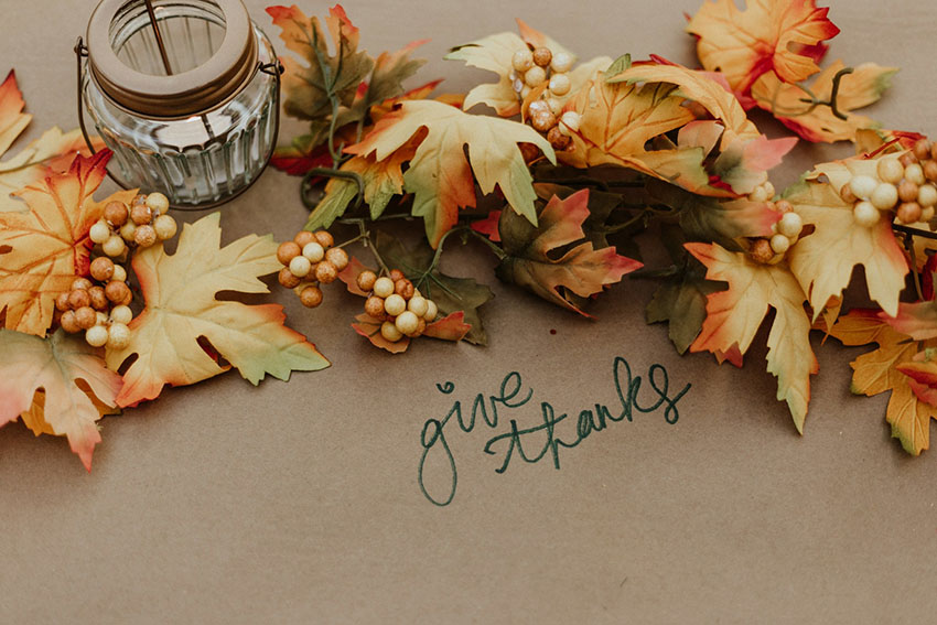 a fall garland made out of faux leaves a candle and a handwritten message saying give thanks