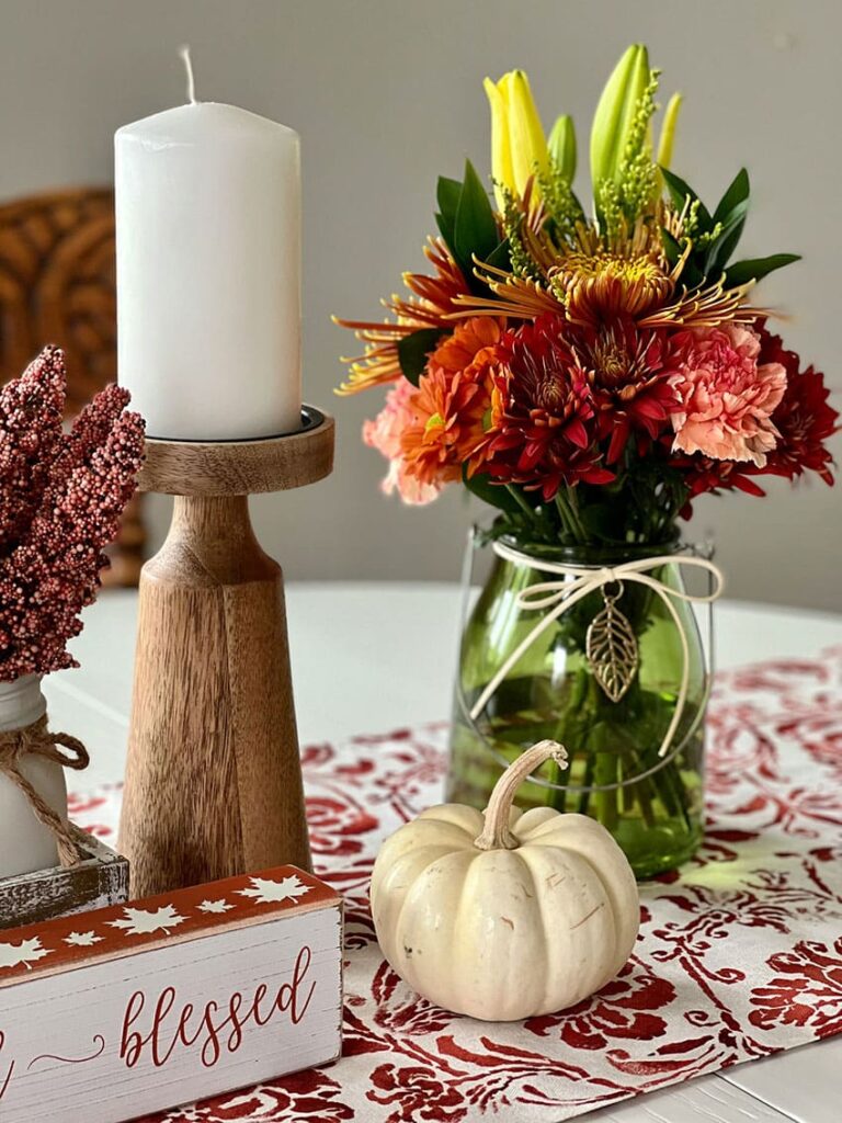 colorful fall decor a vase with fresh flowers a white candle and a white pumpkin