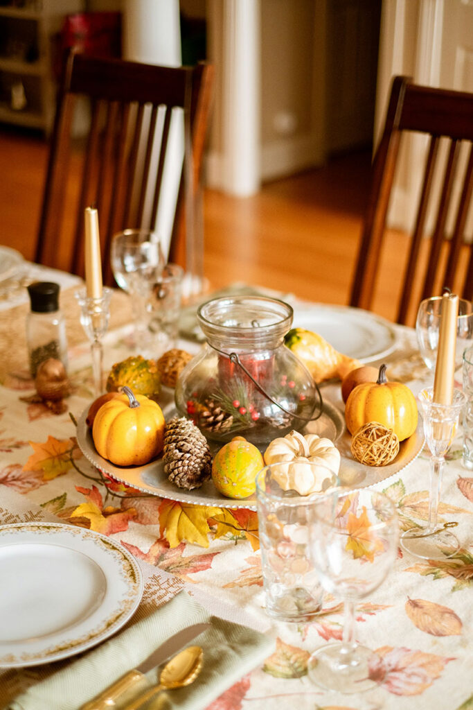 a fall centerpiece made out of decorative pumpkins, and pinecones there is a glass vase in the middle filled with more small pinecones, pine needles and red berries