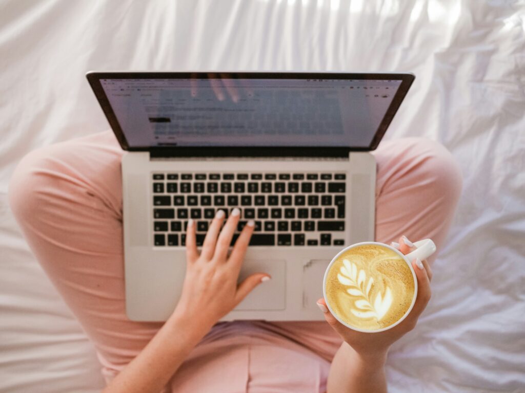 a woman typing in a laptop and holding a coffee cup